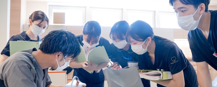 診療室で先輩歯科医師を囲んで実習する研修歯科医｜単独型歯科医師臨床研修プログラム｜やまむら総合歯科・矯正歯科