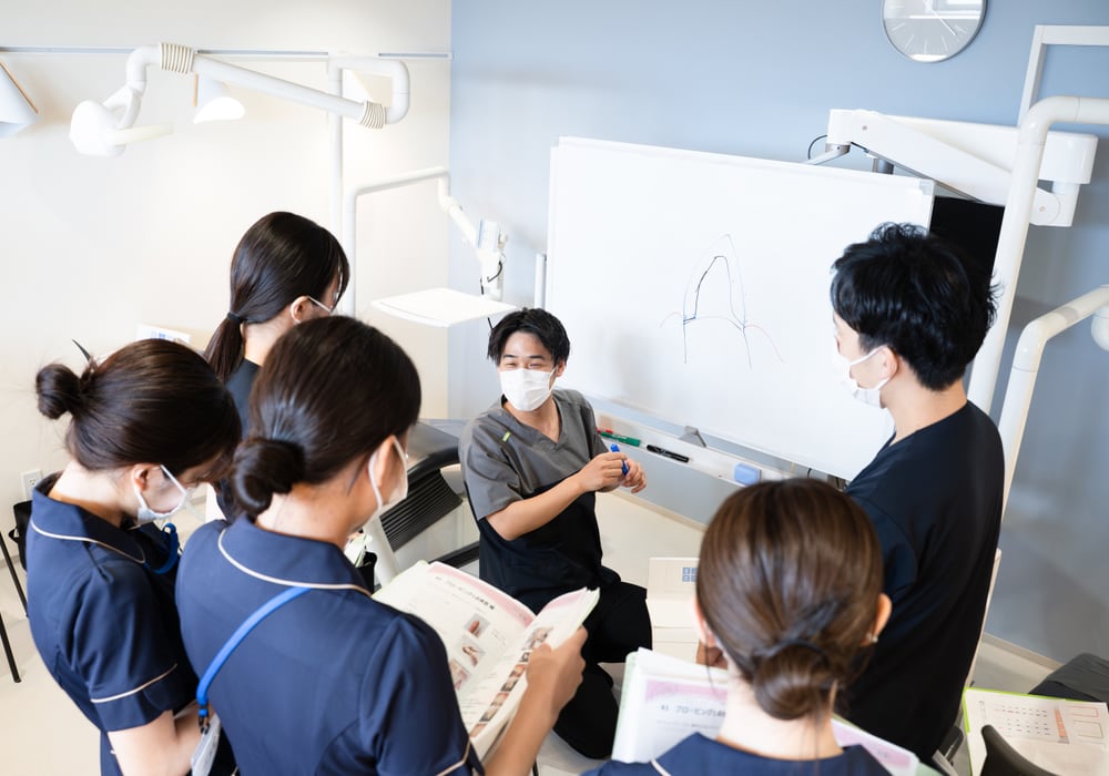 チェアサイドでホワイトボードを使い指導する歯科医師とスタッフ｜臨床研修の現場